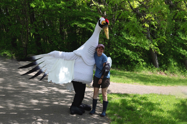 Whooping Crane mascot Hope and and International Crane Foundation aviculturist wearing a blue shirt and wading boots.