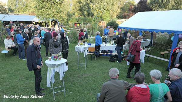 Conference participants gather outside on a green lawn with food and drink. Text: Photo by Anne Kettner