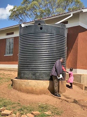 A large steel rainwater tank collects water from a roof in Uganda.