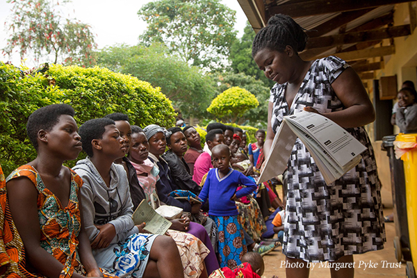 A woman shows materials to a group of women and children in Uganda. Photo by Margaret Pyke Trust