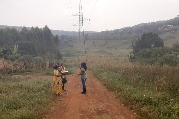 Several people stand below a powerline in Uganda.